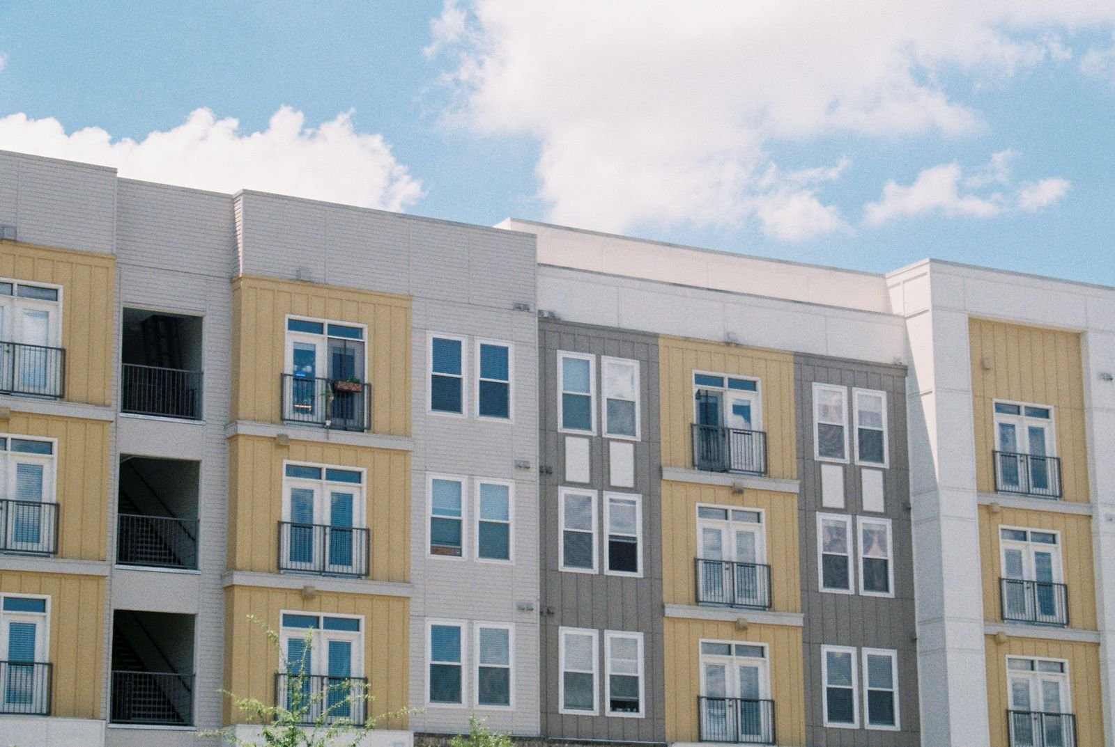 Four-storey apartment building with yellow and grey panels and balconies under a blue sky