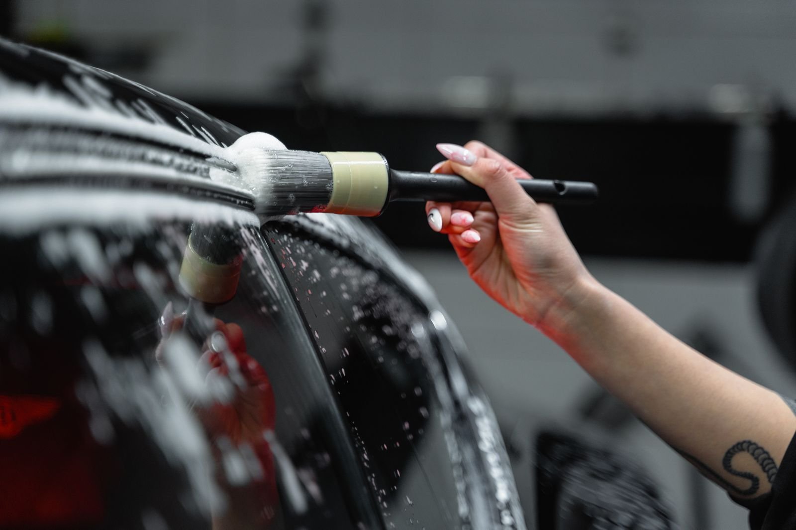 Hand brushing soap foam on a dark car at a car wash