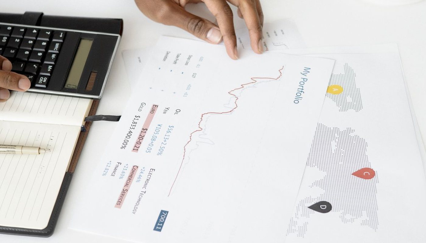 Hands using a calculator beside printed charts and a notebook