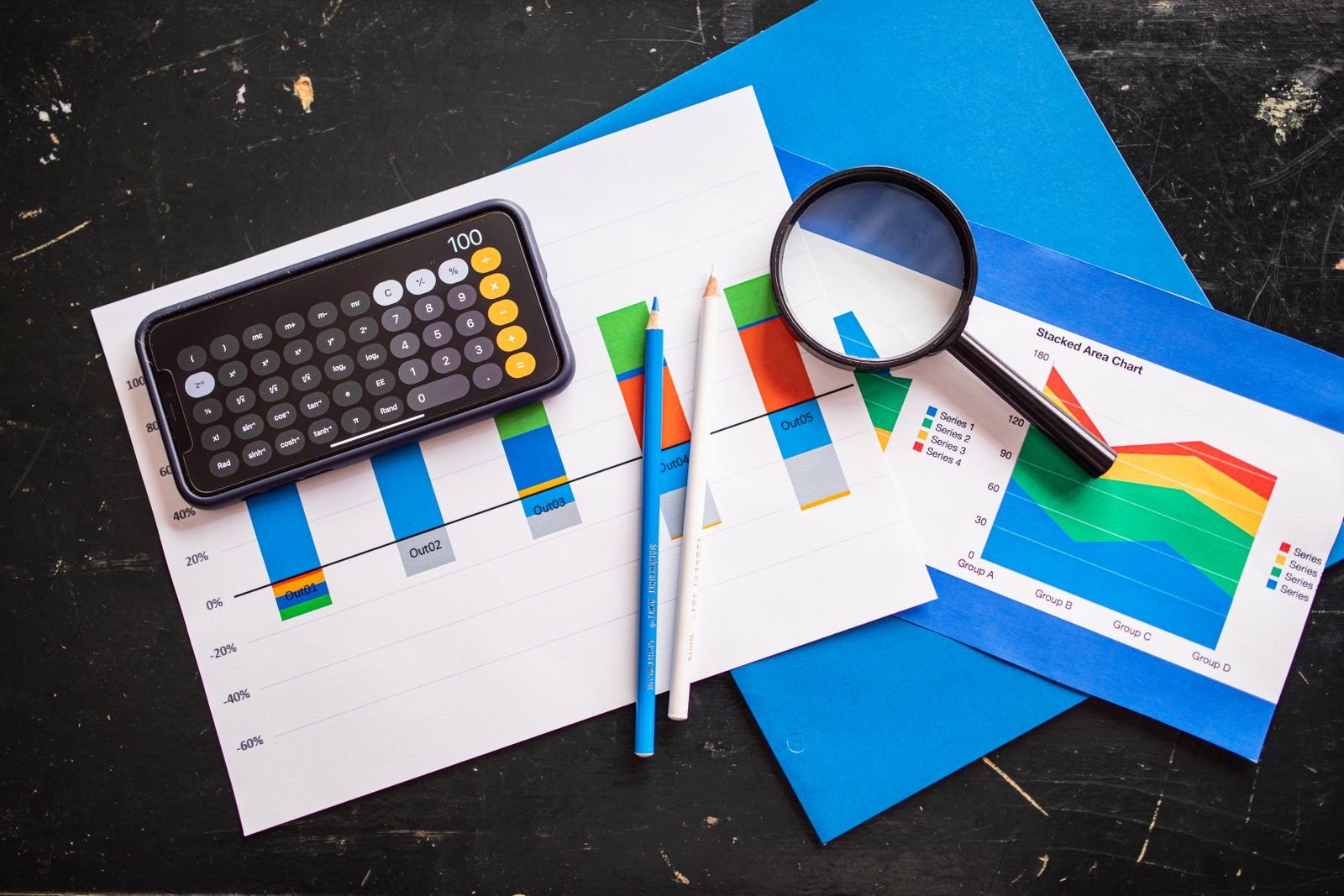Calculator, pens, a magnifying glass and printed charts on a dark desk