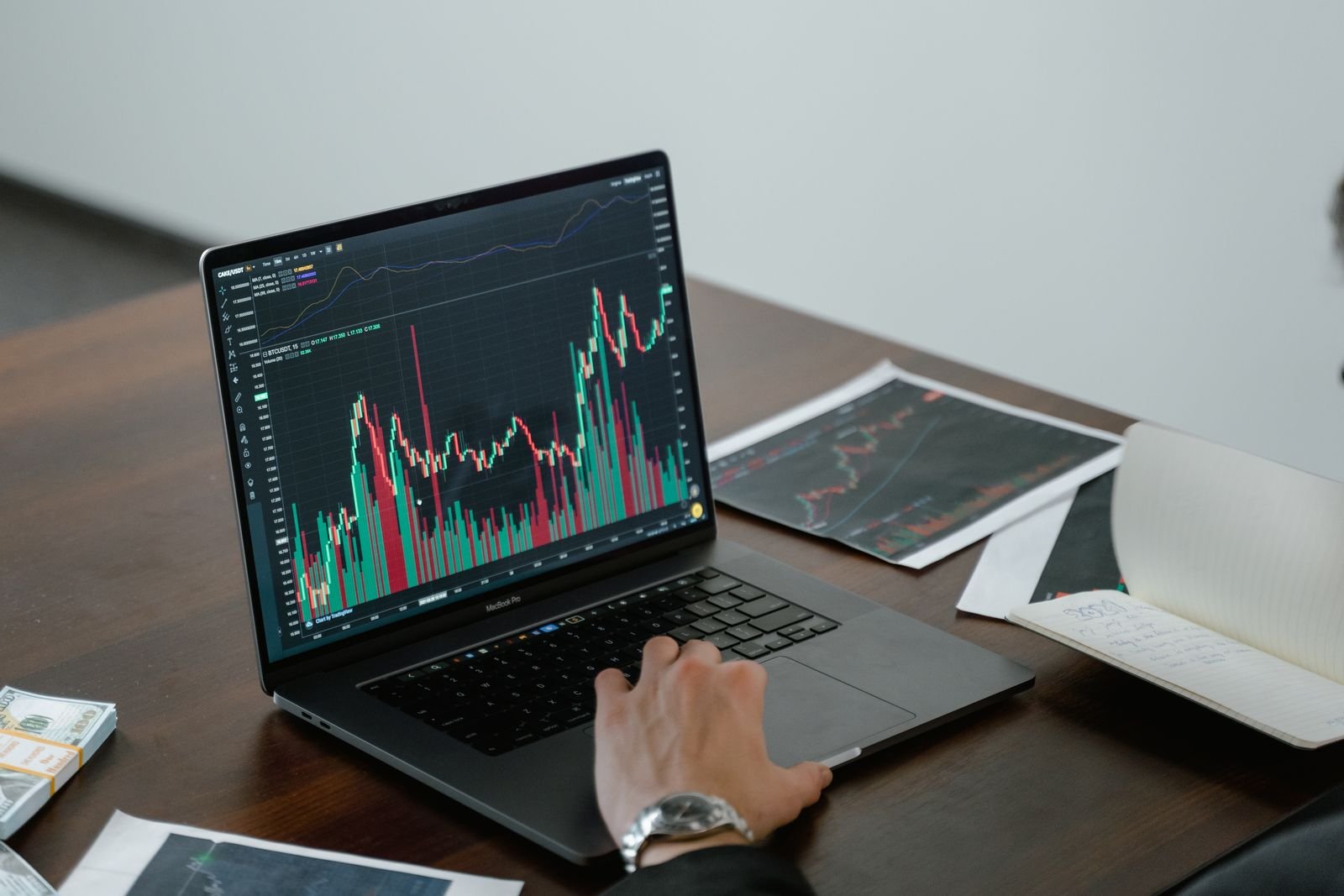Laptop showing financial charts on a desk beside printed reports
