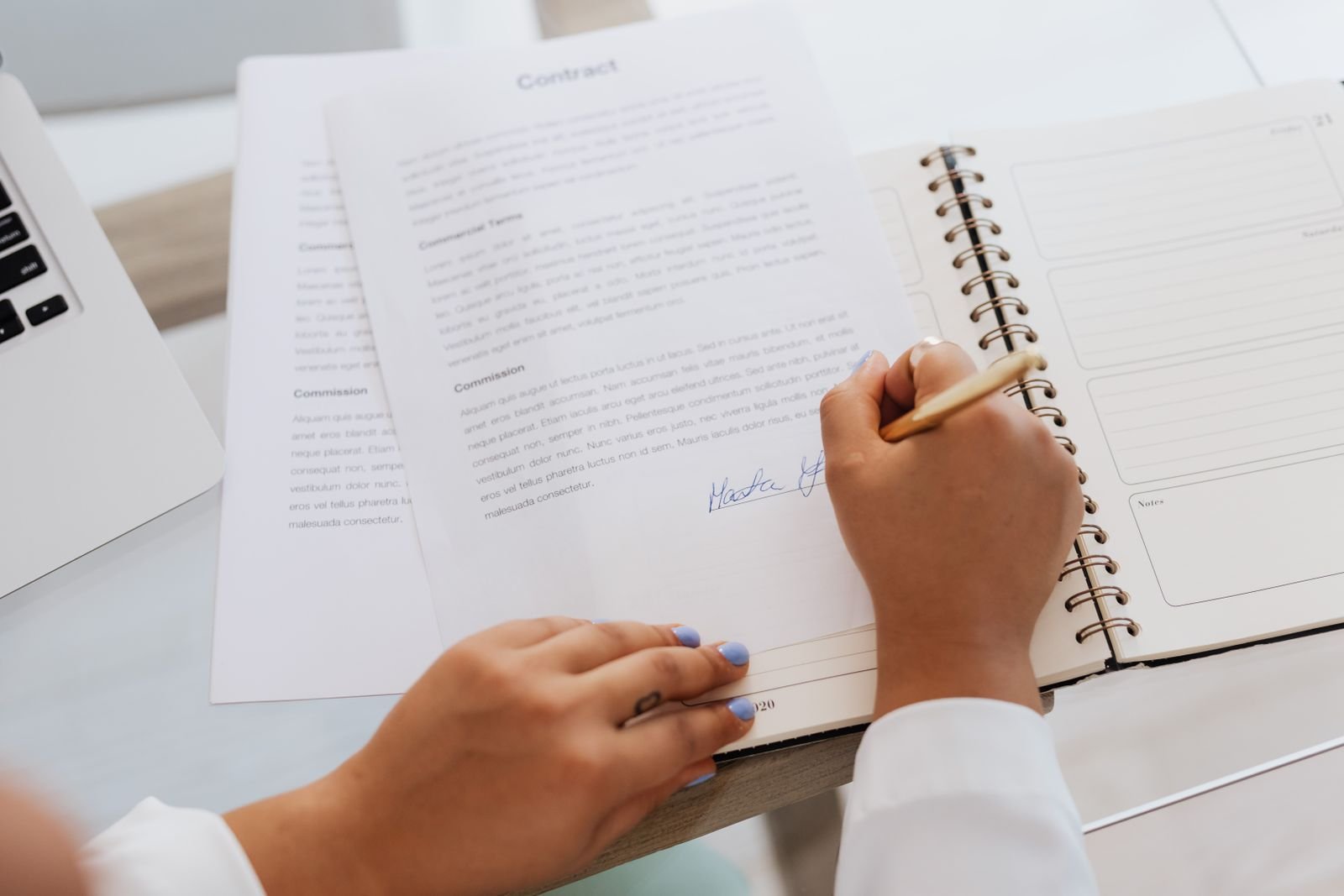 Person signing a contract with a pen beside an open notebook