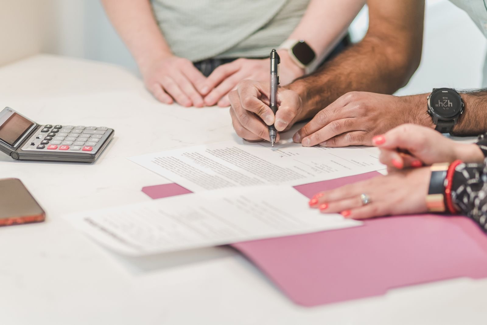 People signing loan paperwork beside a calculator on a white table