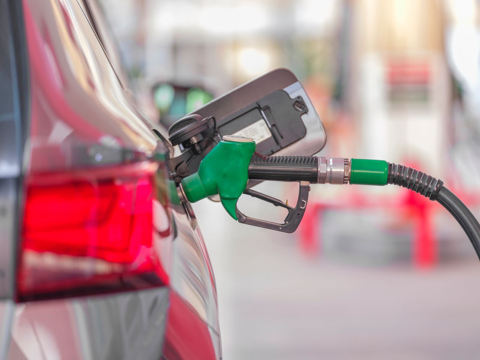 Green fuel nozzle refuelling a red car at a gas station