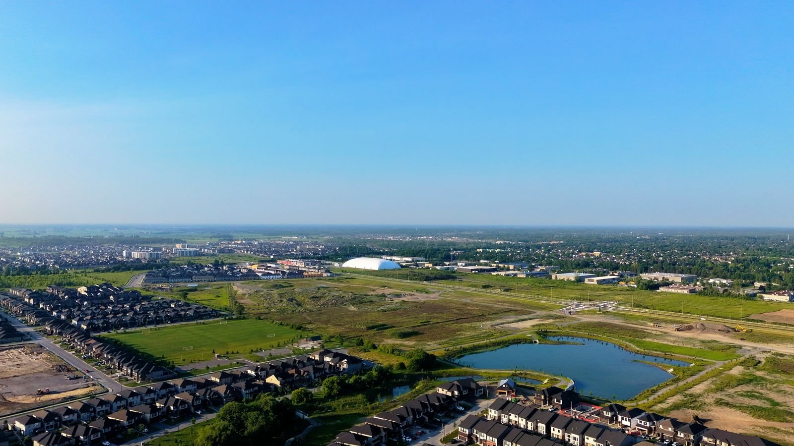 Aerial view of a suburban development beside open land and a pond