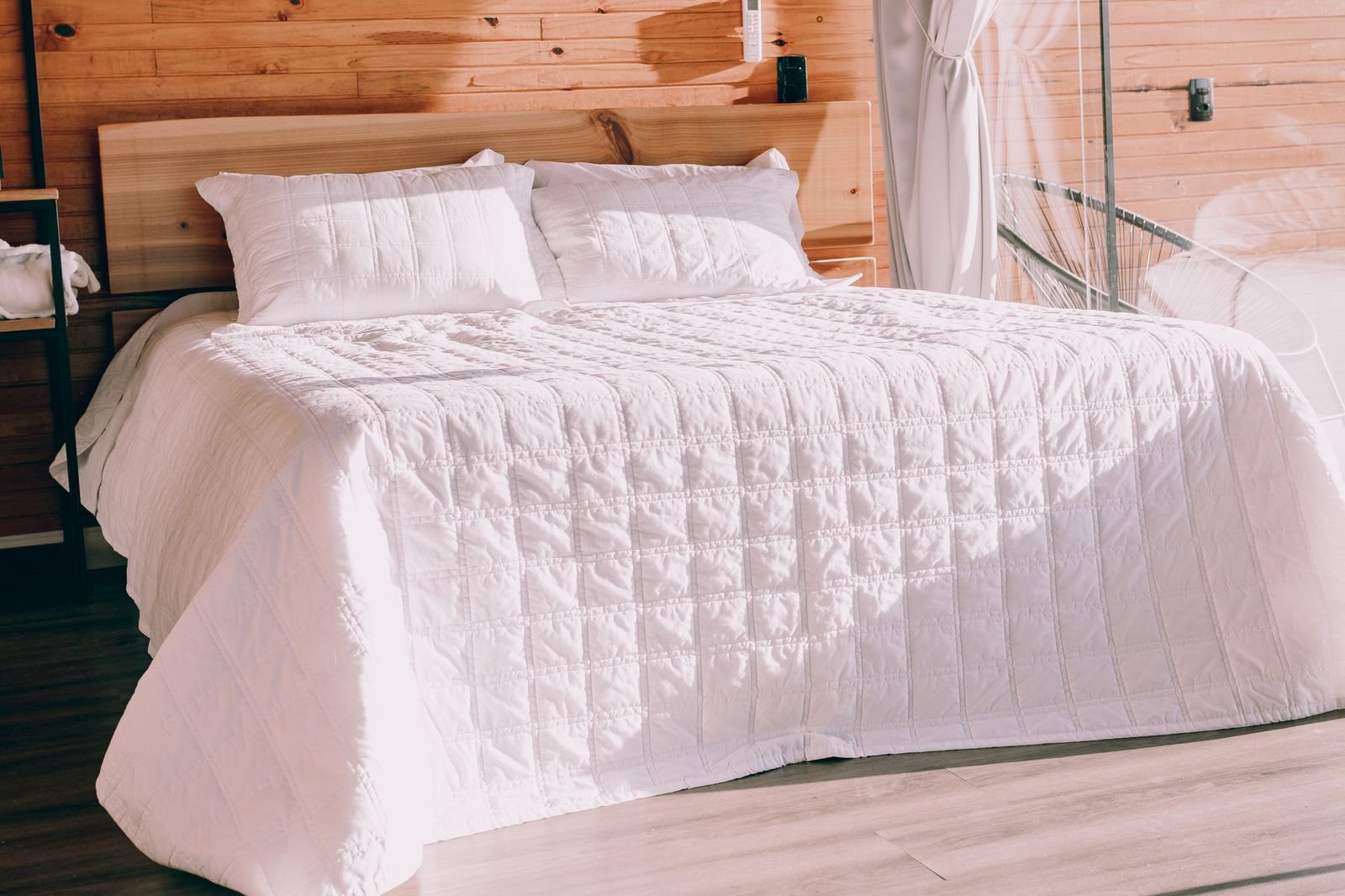 Neatly made hotel bed with white bedding and a wood-panelled headboard