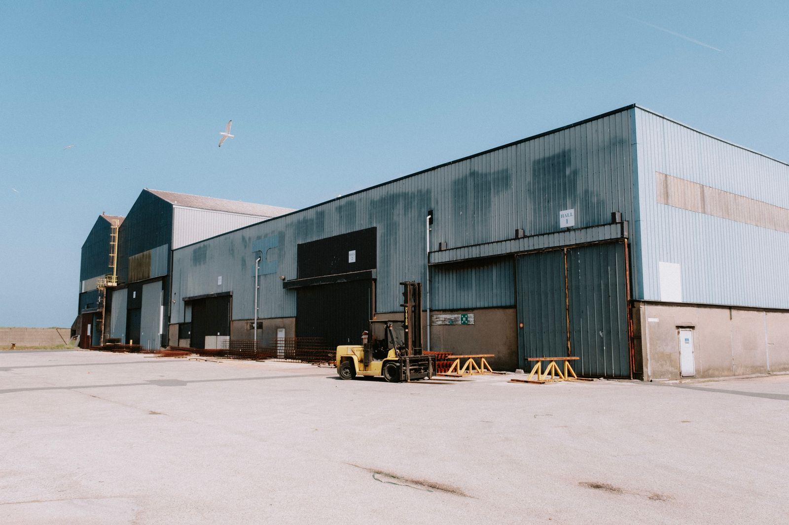 Large industrial warehouse building with loading doors and a forklift in the yard