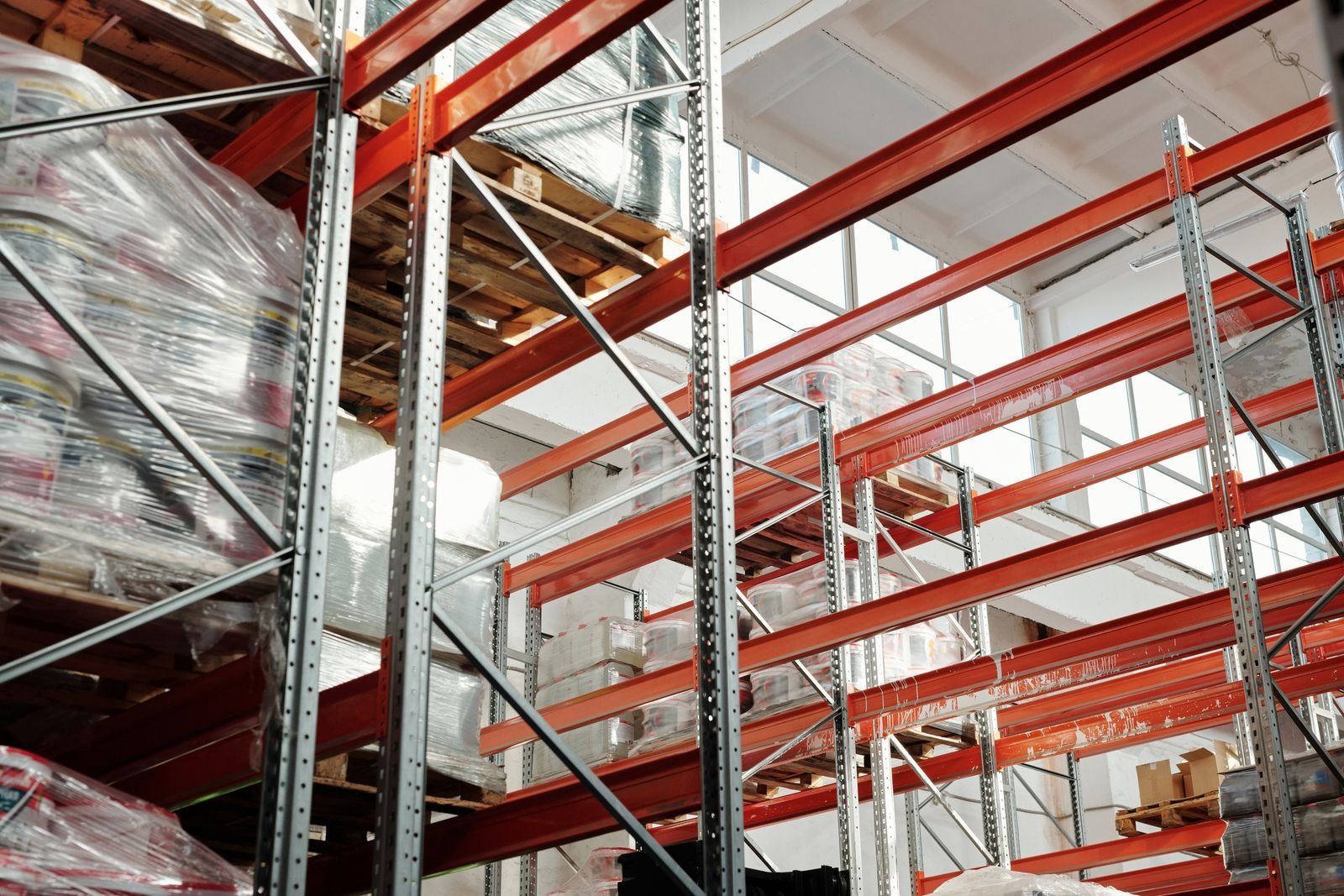 Red and grey warehouse racking loaded with pallets under skylights
