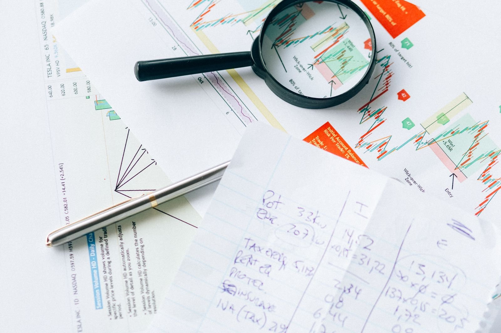 Financial charts, handwritten calculations and a magnifying glass on a desk