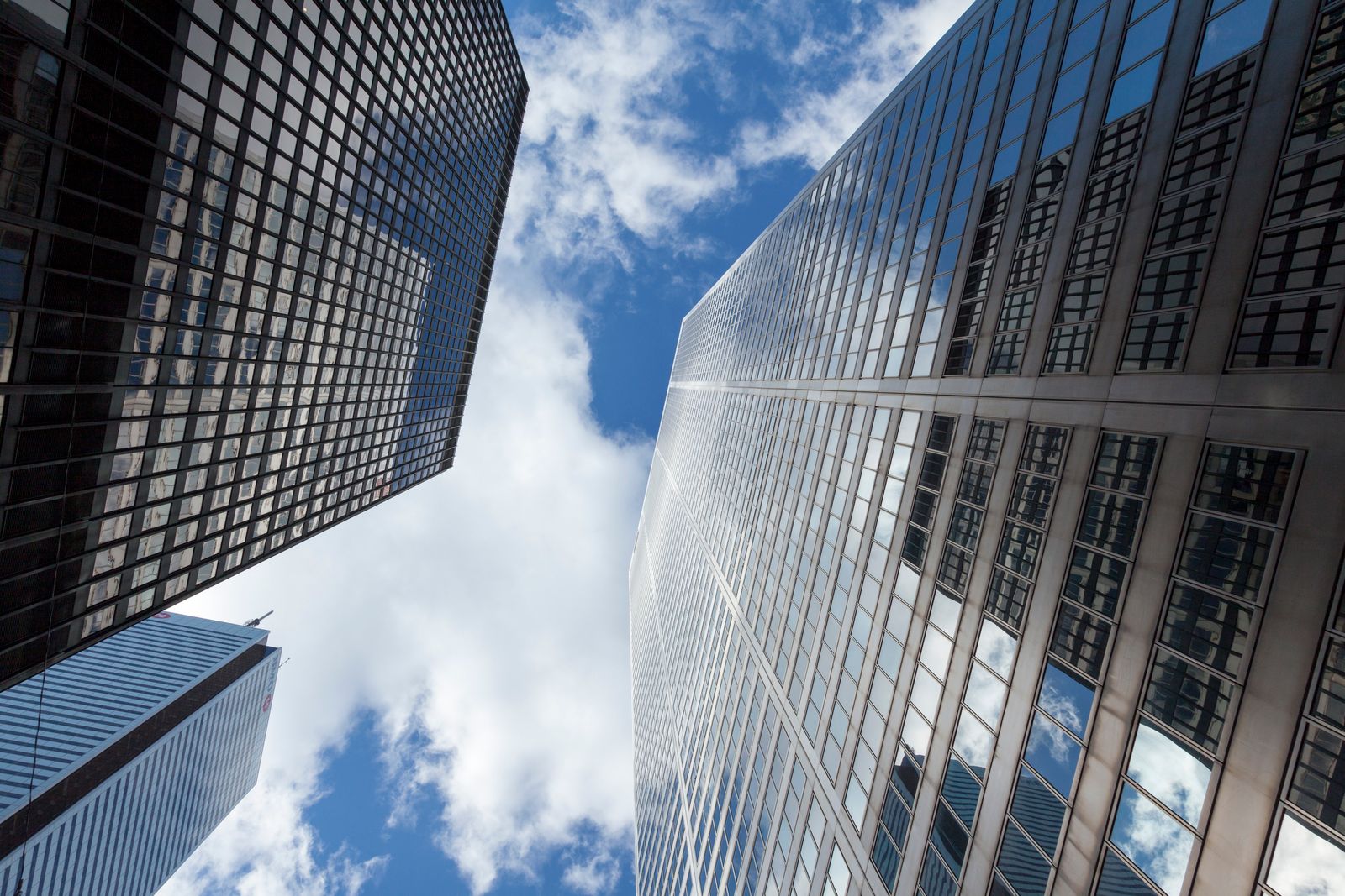 Glass office towers seen from street level against a blue sky with clouds