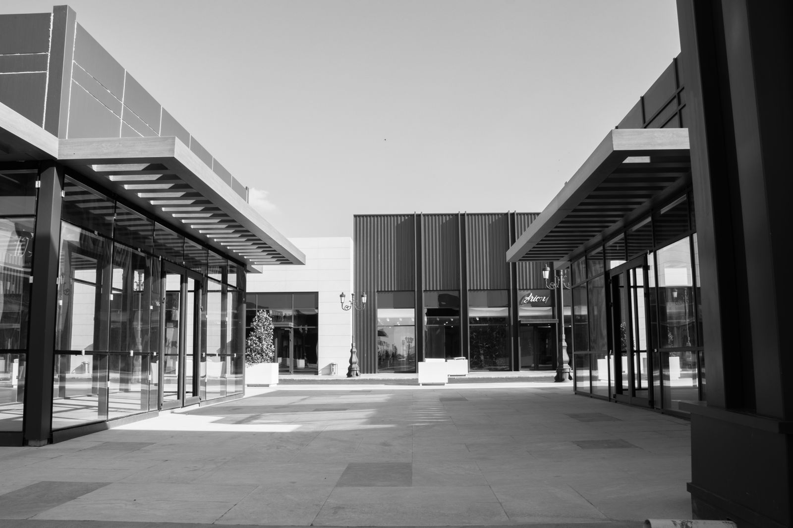 Black and white view of a modern retail plaza courtyard with glass storefronts