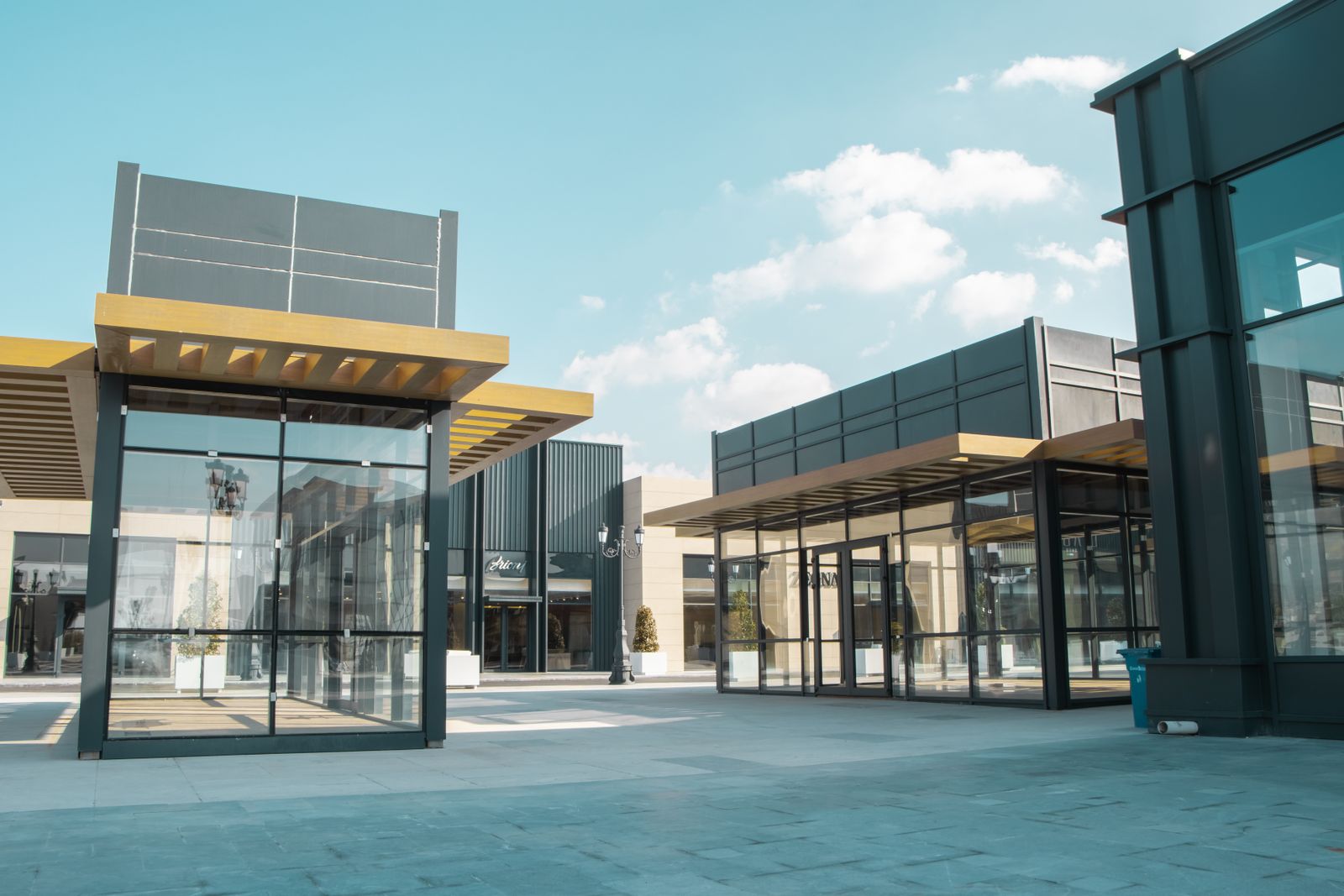 Modern retail plaza with glass storefronts and covered walkways under a blue sky