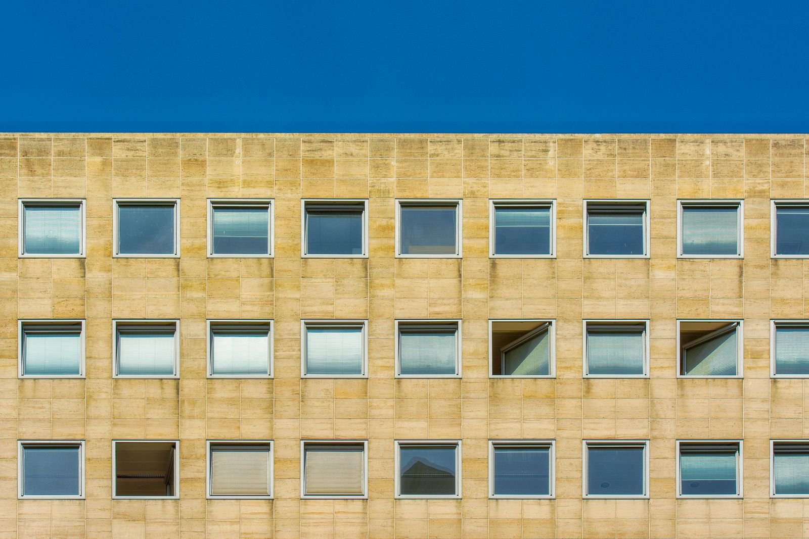 Sandstone-coloured commercial building facade with rows of windows under a blue sky