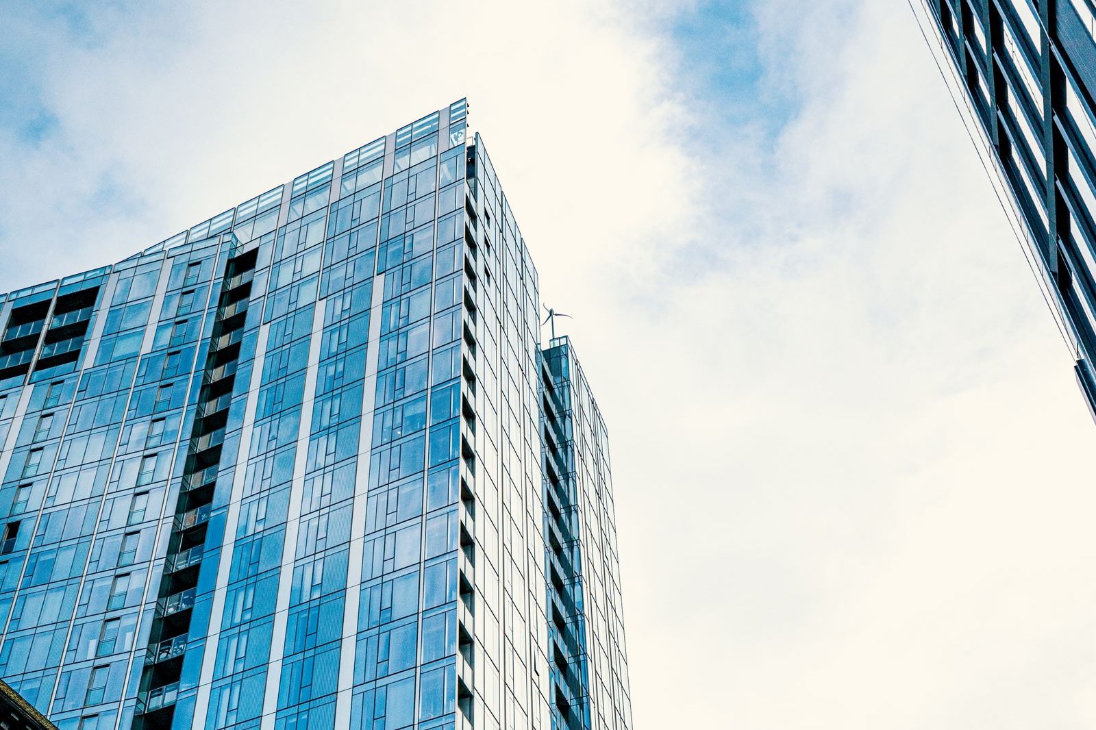 Blue glass office tower seen from below against a cloudy sky