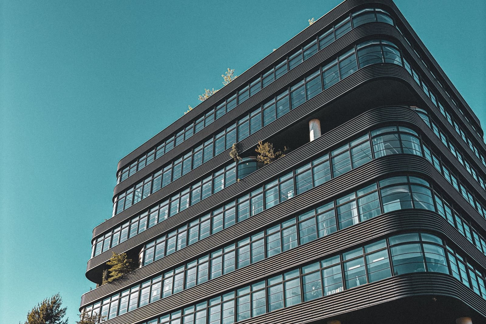 Modern dark glass office building with curved terraces against a teal sky