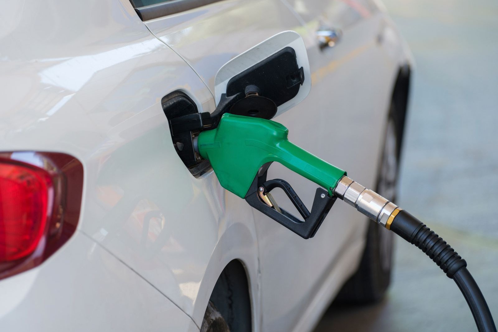 Green fuel nozzle refuelling a white car at a gas station